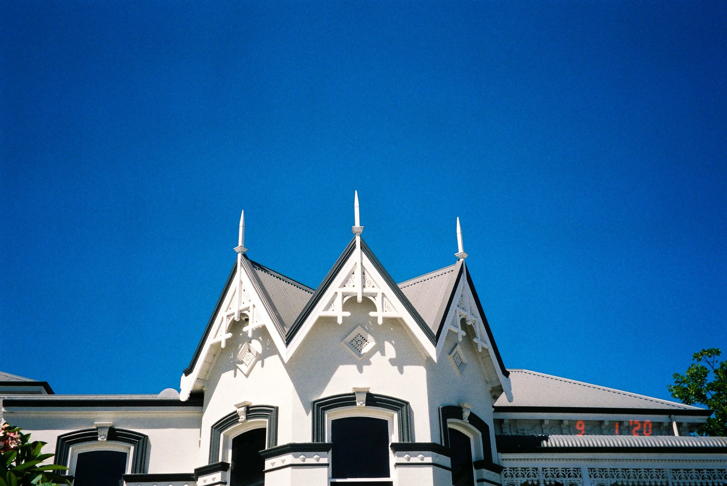 White Victorian-style house with ornate detailing and pointed roofline, set against a clear blue sky.