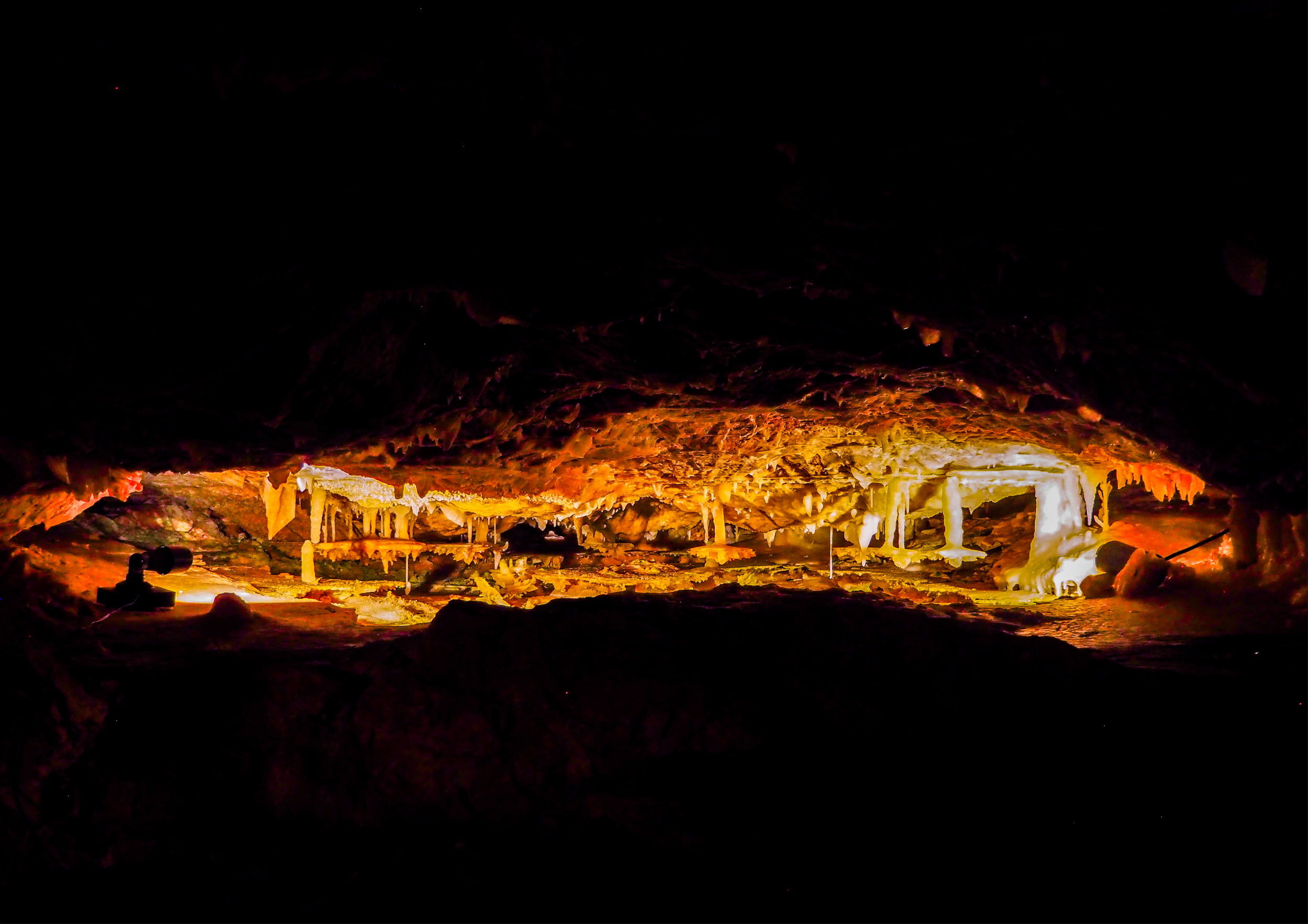 Underground cave with stalactites and stalagmites illuminated by warm lighting.