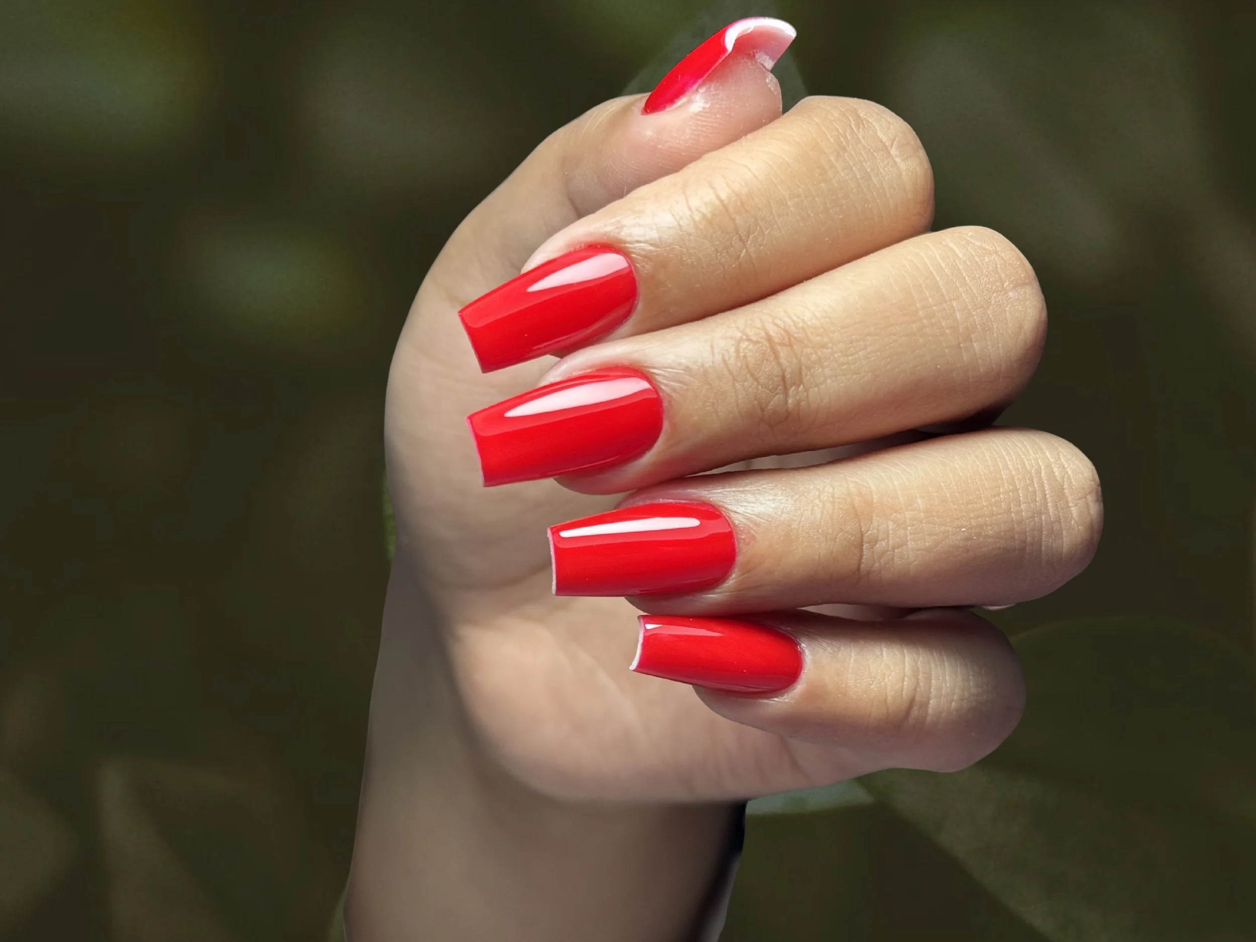 Uña pintada de rojo con esmalte brillante, en un dedo de mano, con fondo borroso