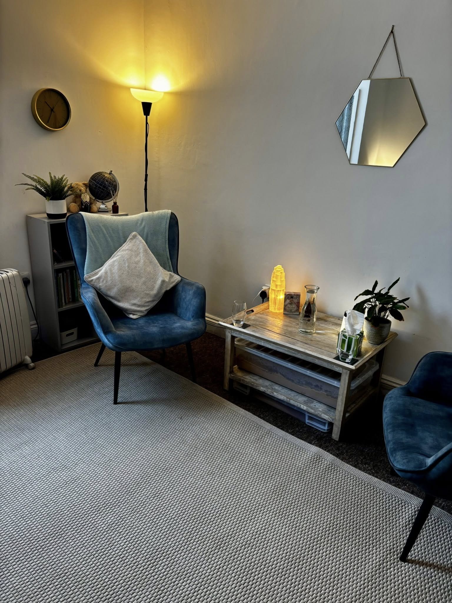 Picture showing the chairs of a counselling room. Their is a table between the chairs with a lamp glowing softly giving the space a cozy feel.