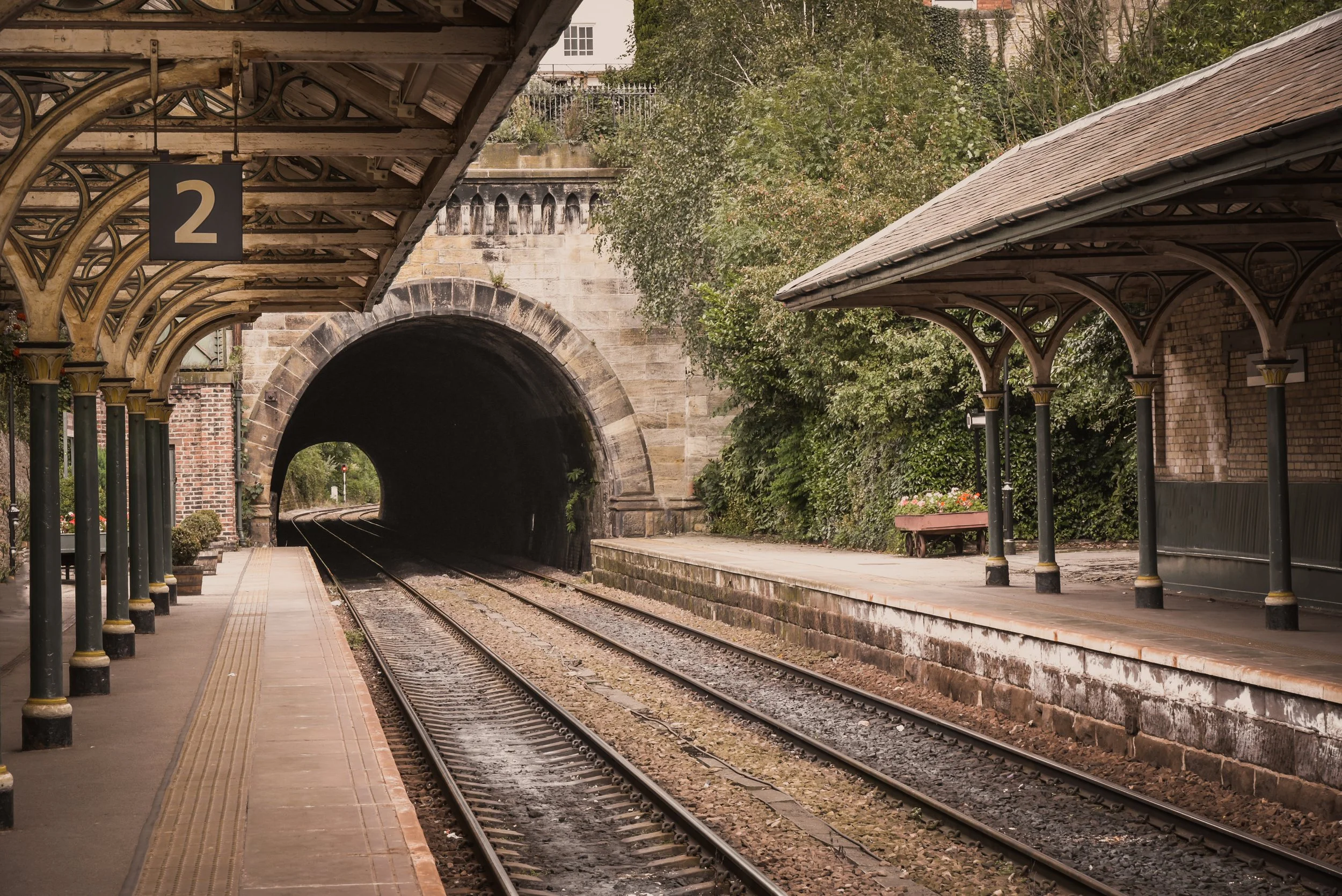 Empty train station platform with a tunnel in the background and a roofed shelter on the right side.
