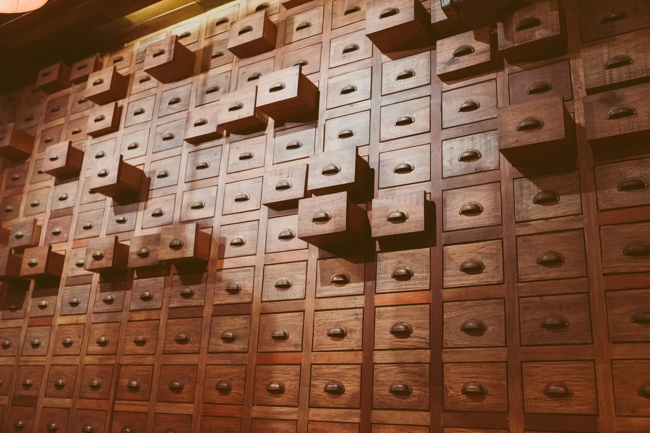 A wall of small wooden drawers arranged in a grid pattern with some drawers open, showing dark handles.