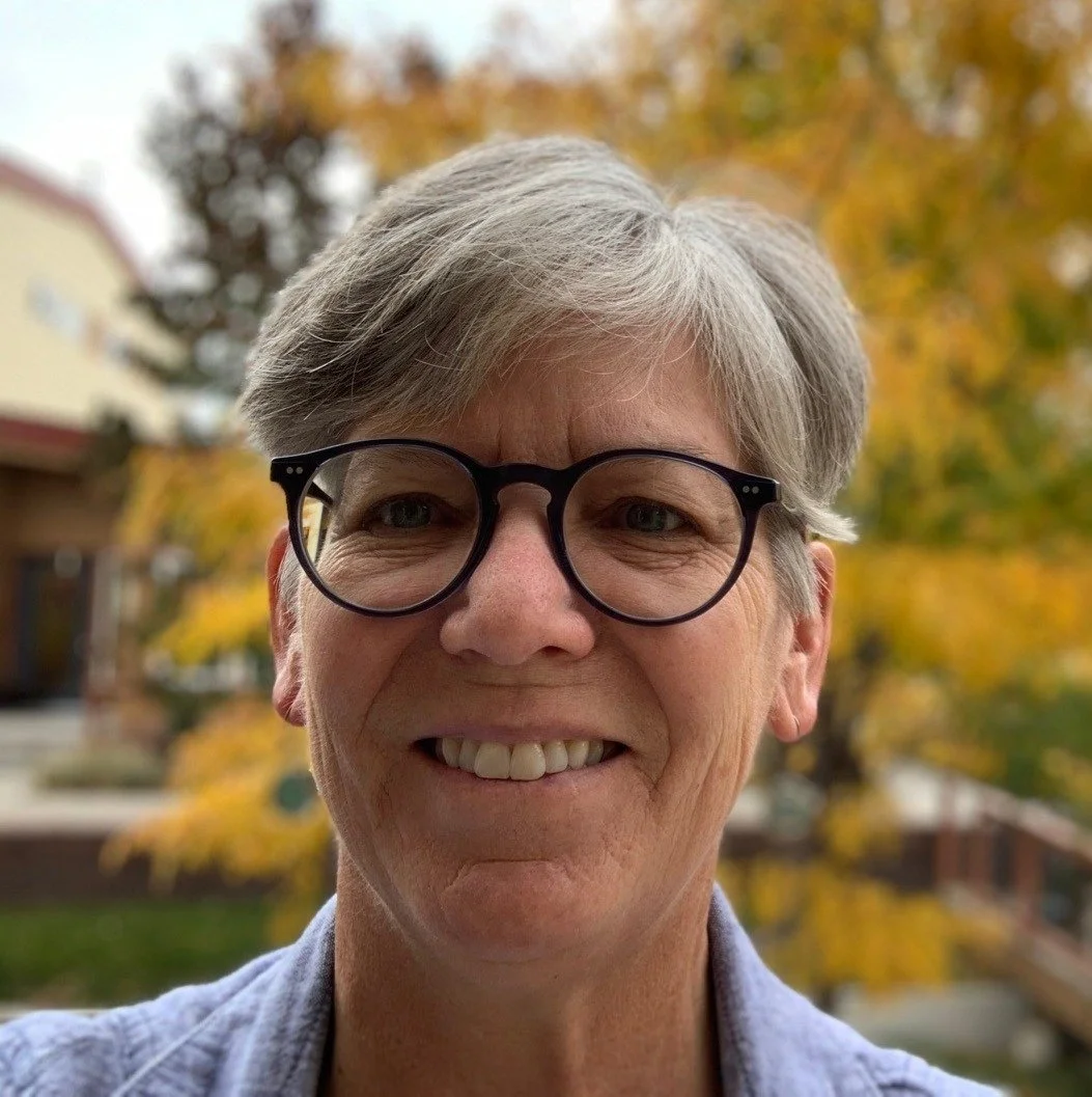 Therapist Patty Podhaisky with short gray hair and black glasses standing outside with autumn leaves in the background.