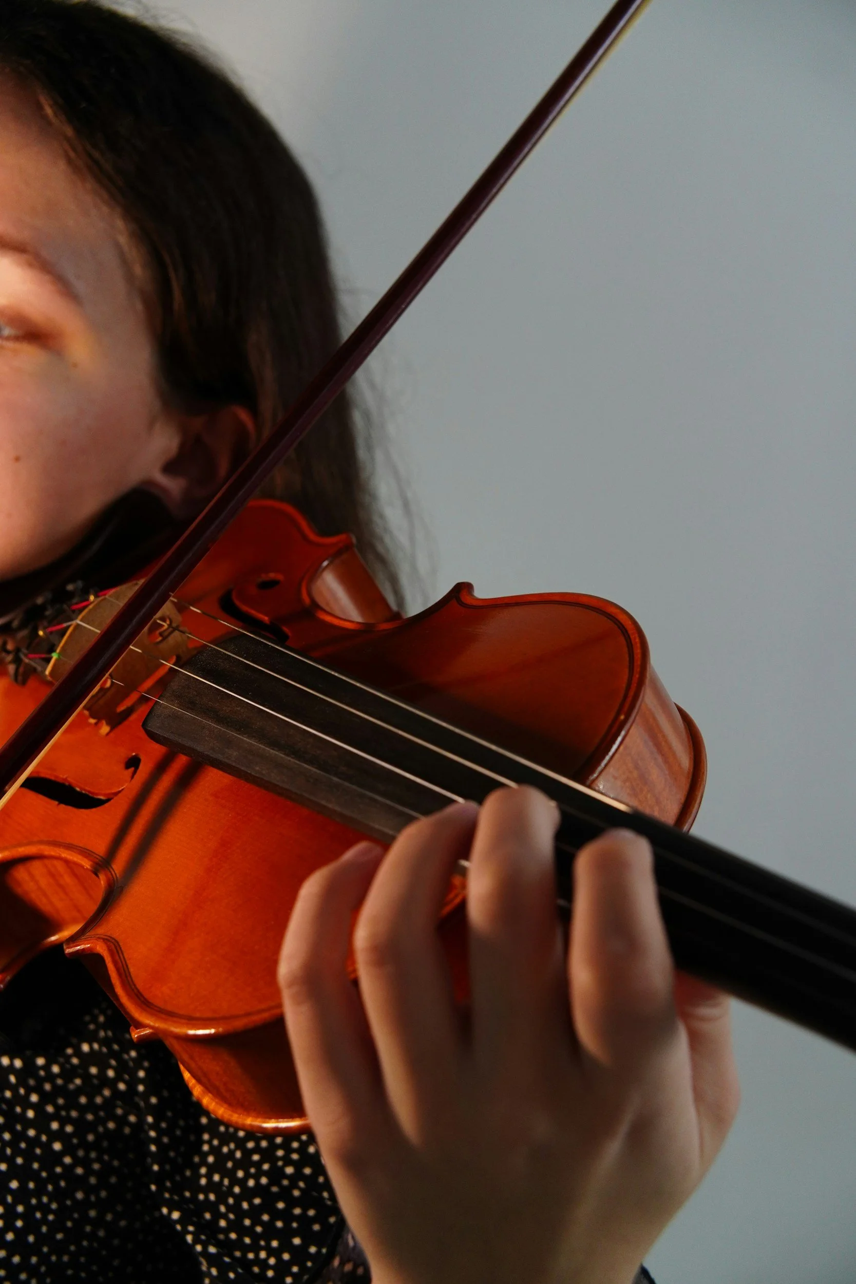 A young person playing a violin, focusing on their hand on the fingerboard and the bow.