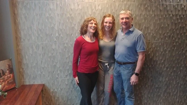 Heidi Brown's family standing together, smiling, against a textured wall.