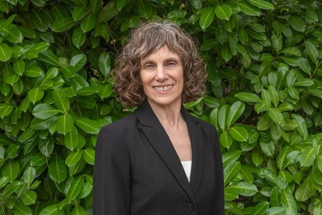 Heidi Brown standing outdoors in front of green leafy plants, smiling at the camera.
