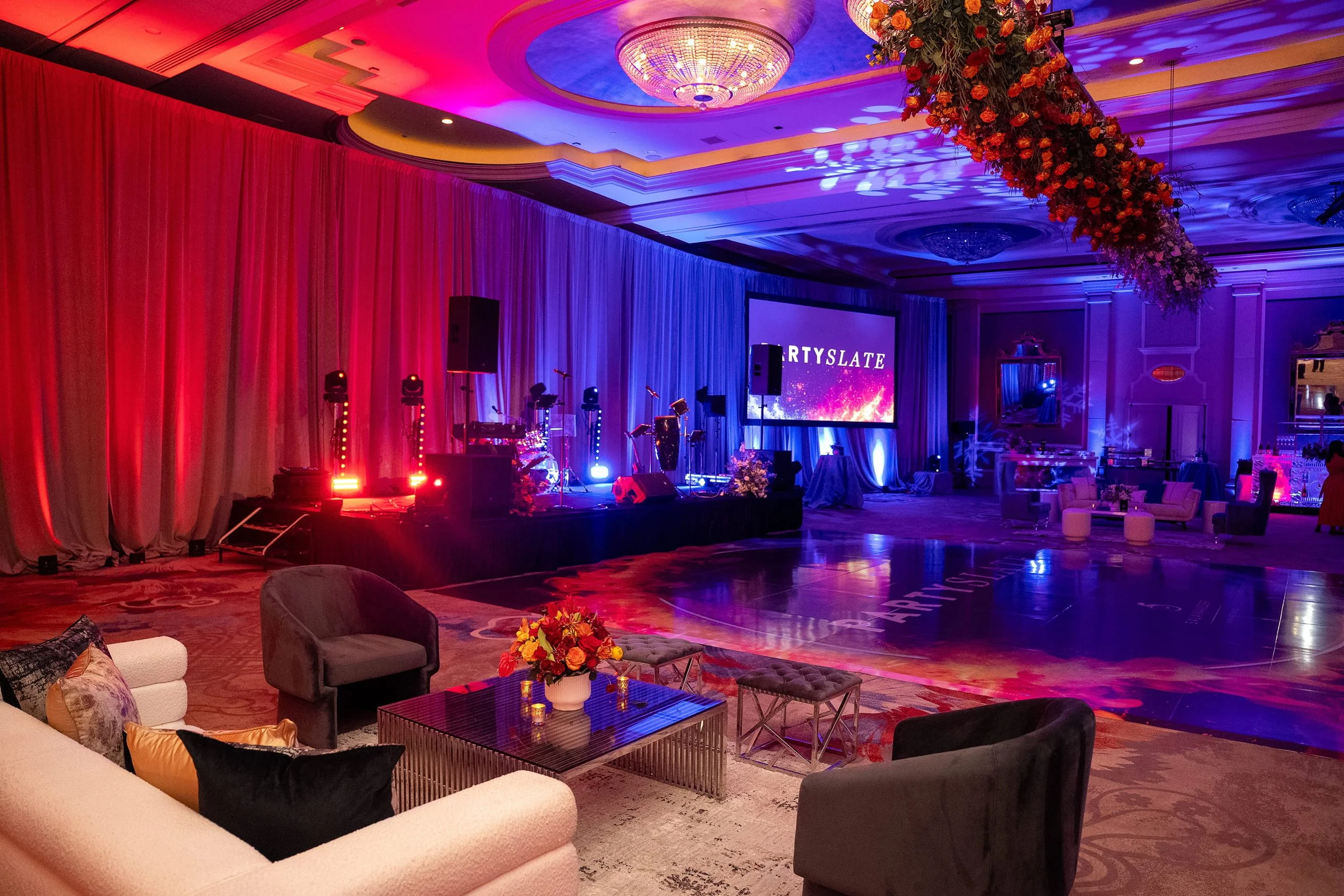 Ballroom event setup with red and purple uplighting, projection screen, and stage produced by RDAV