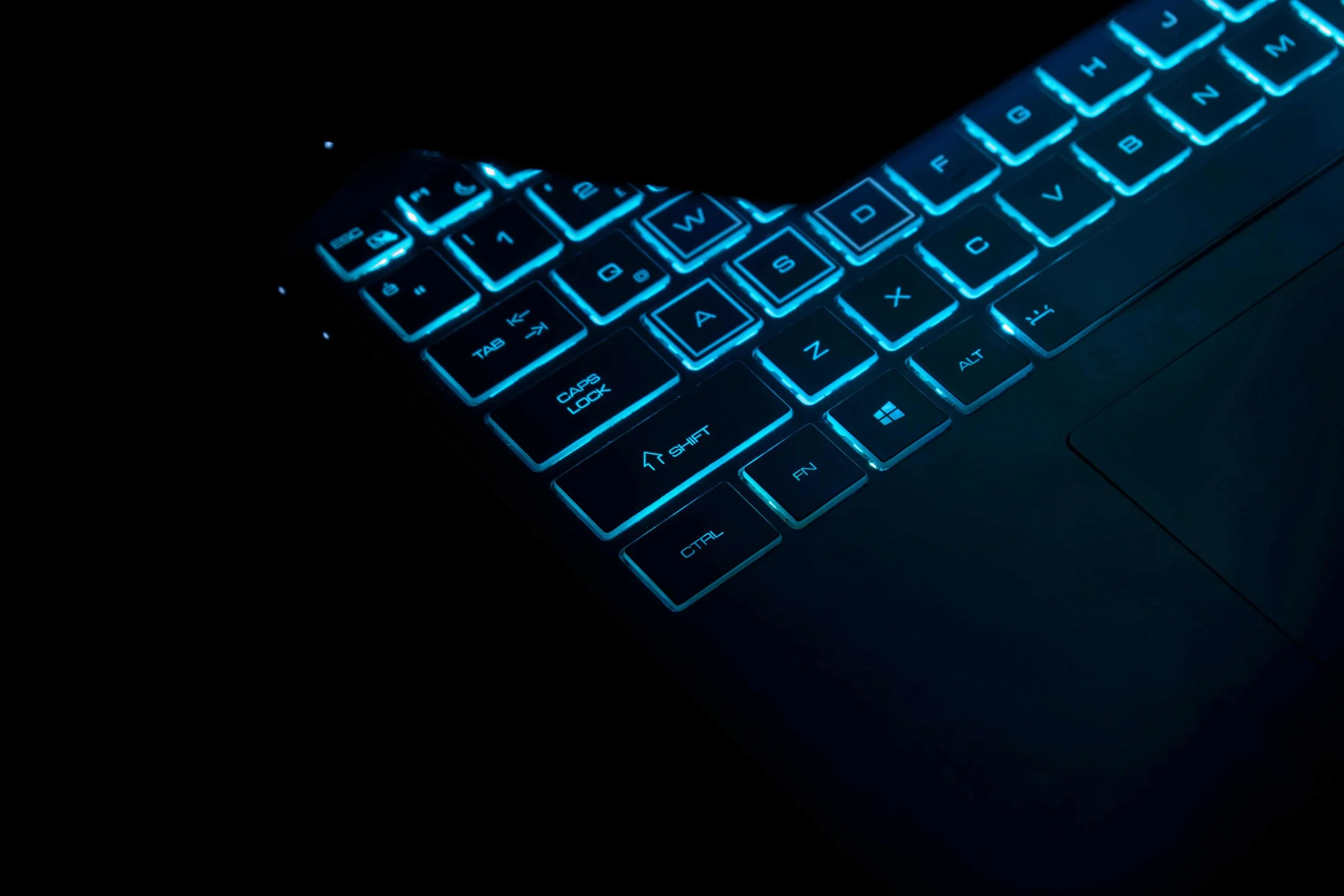 A laptop keyboard illuminated with blue backlight keys in a dark environment.