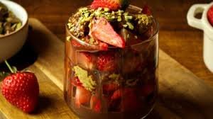 A glass jar filled with mixed berries and topped with whipped cream, with strawberries and other bowls of berries nearby.