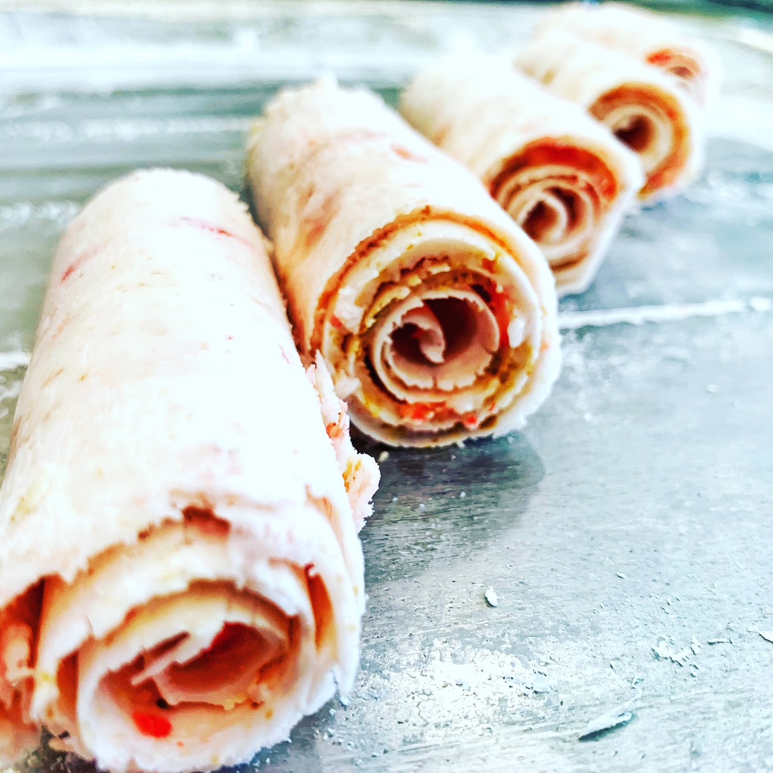 Four rolled crepes with toppings on a metallic surface.