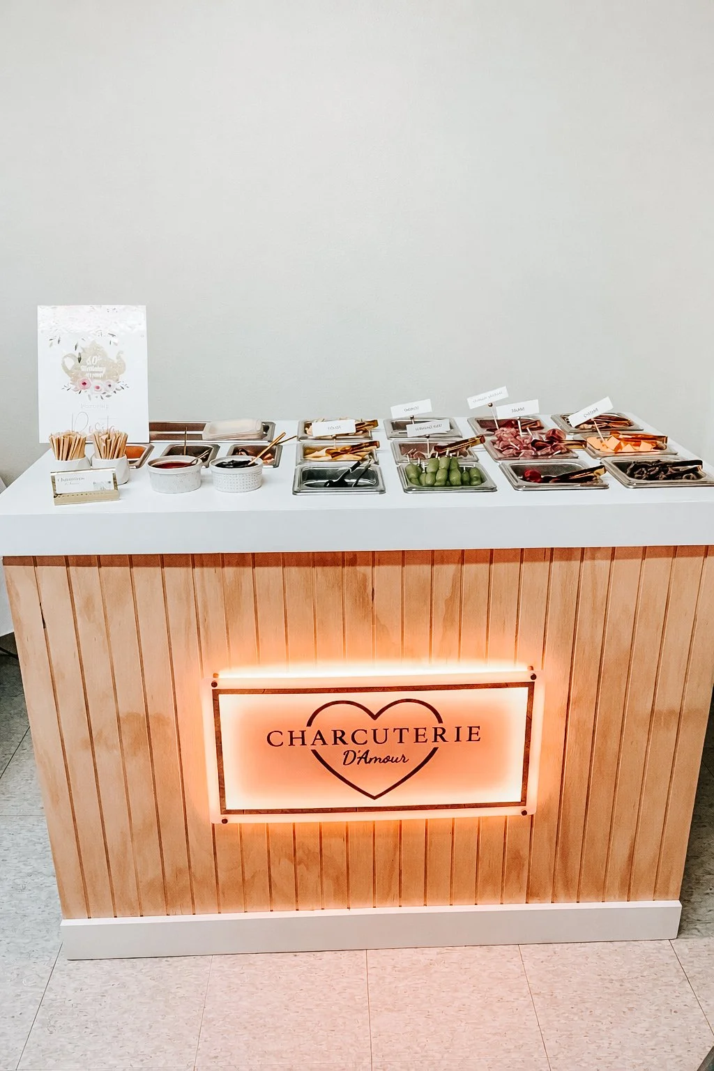 A breakfast or brunch station with various toppings and ingredients, labeled in French, in a wooden and white display with heart graphic and text 'Charcuterie D'Amour'.
