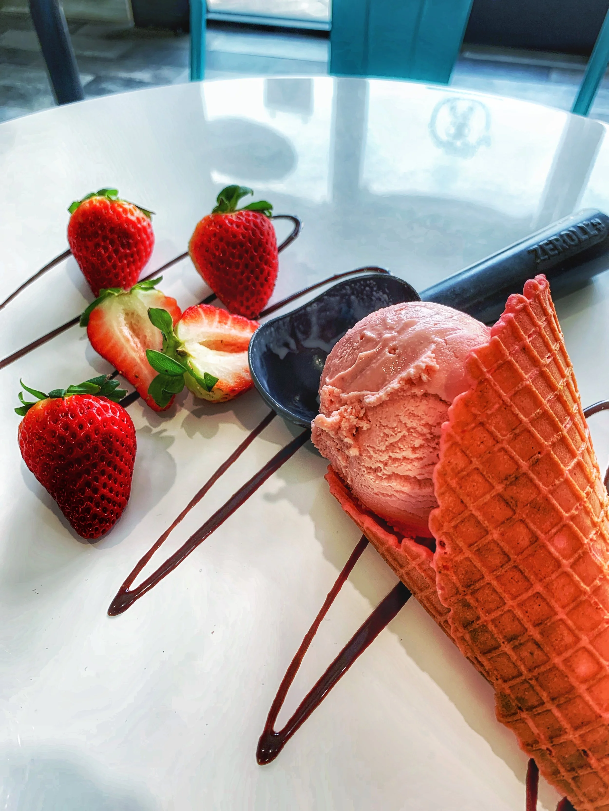 Strawberries and a scoop of strawberry ice cream in a cone with chocolate drizzle on a white plate.