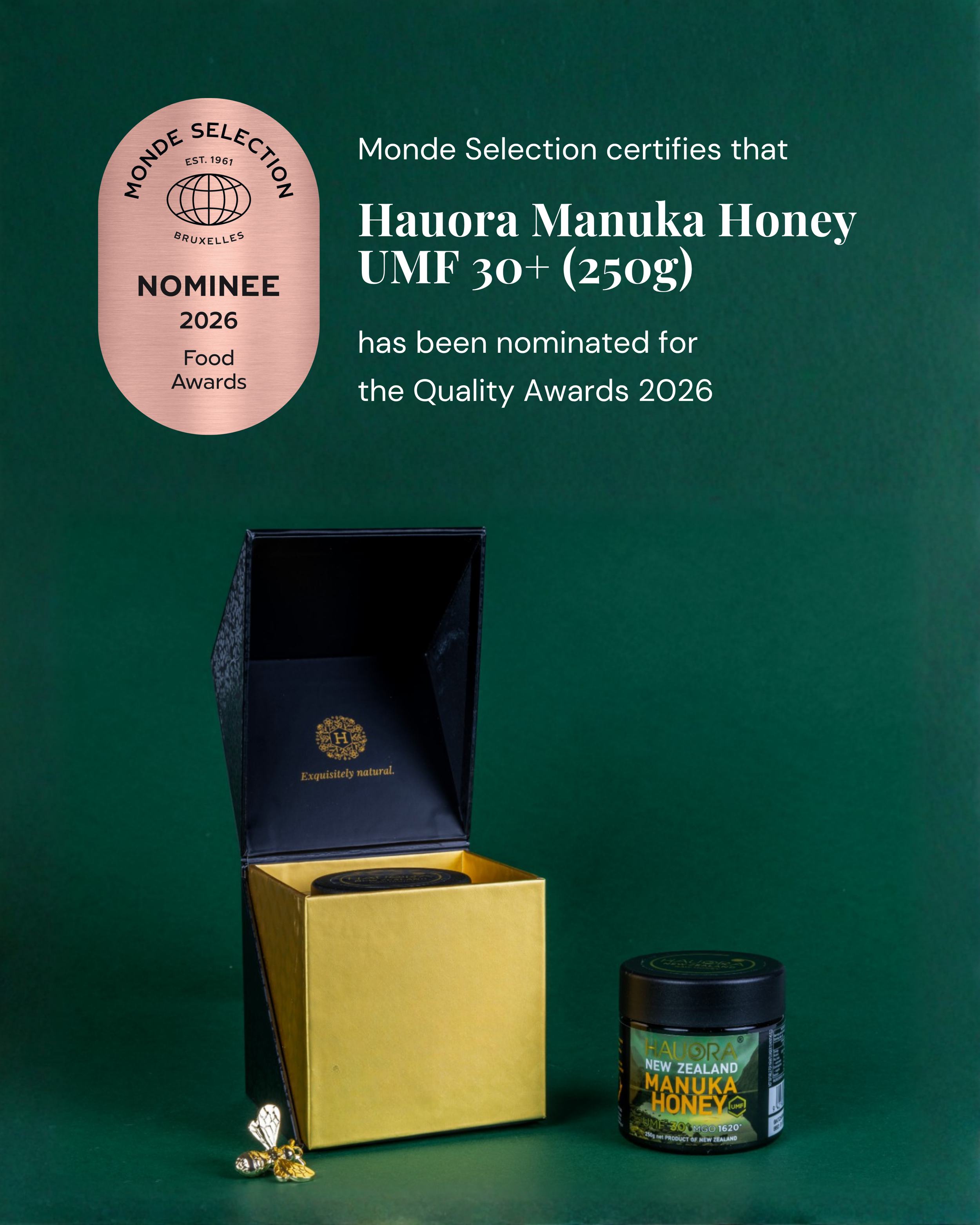 A black container of Hauora Manuka Honey with green, yellow, and black label text, placed on a green surface with a small decorative gold and black bee figurine beside it. Behind the honey is a yellow and black box, and above it, a pink and black Monde Selection certification badge for food awards. The background is green.