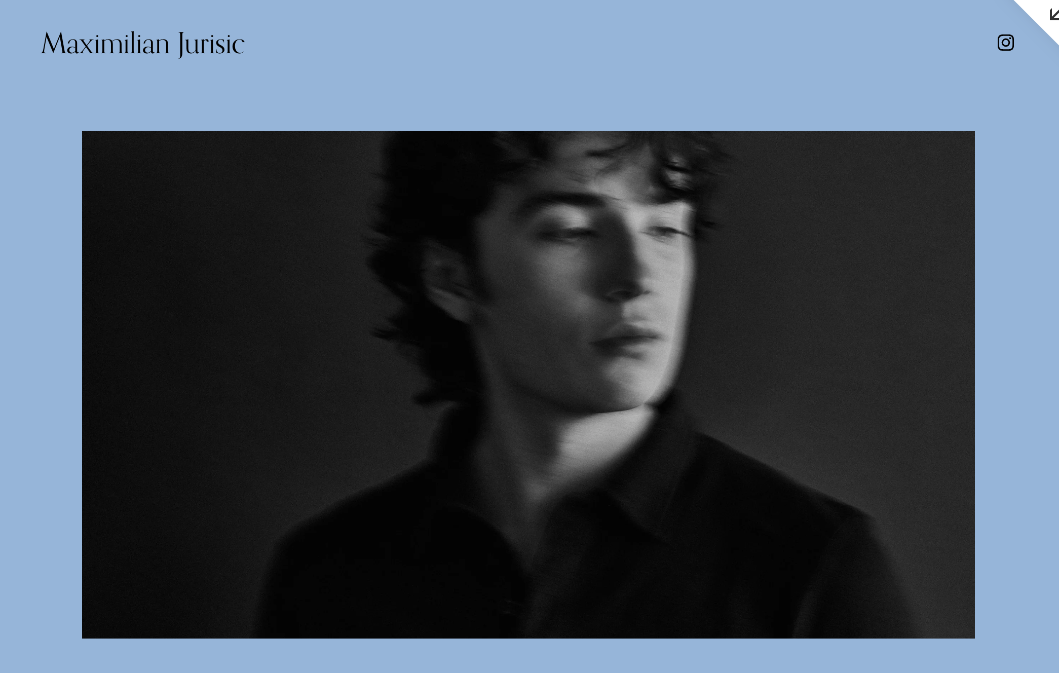 Black and white portrait of a young person with short, curly hair, wearing a dark top, with a blurred background.