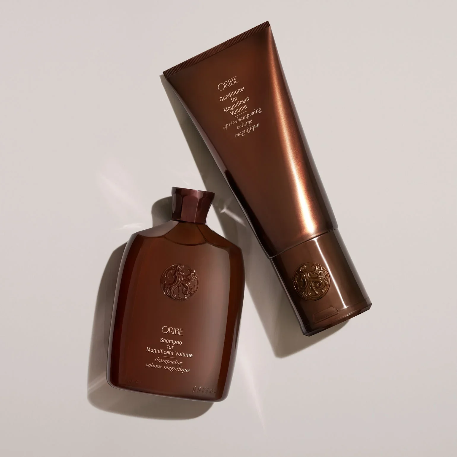 Two brown hair care products from Oribe: a shampoo bottle and a conditioner tube, both with embossed logos.