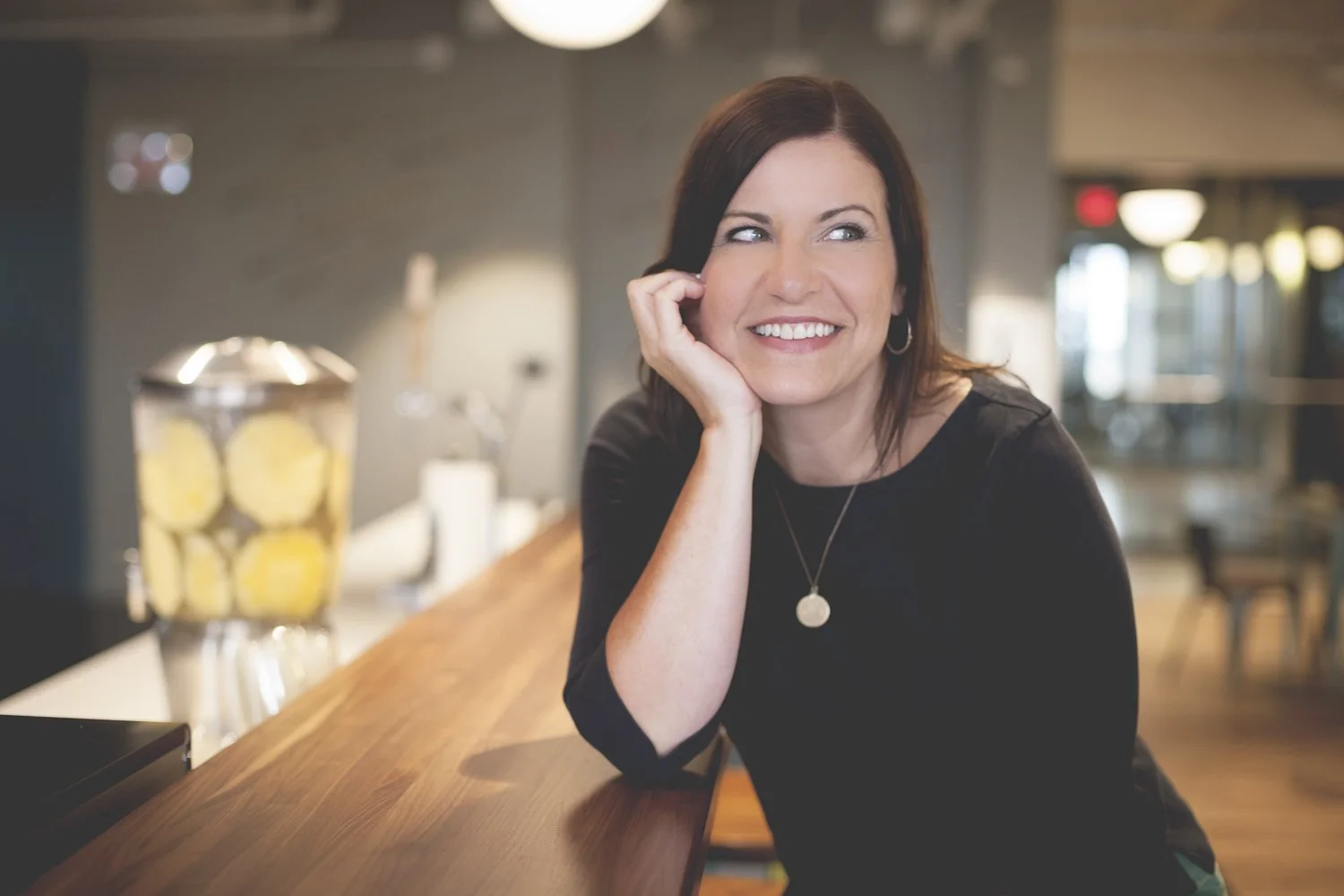 Rachel Muir, a warm and approachable nonprofit fundraising consultant, smiles brightly at a light-filled café, embodying a spirit of generosity and fun, ready to inspire nonprofits to thrive.