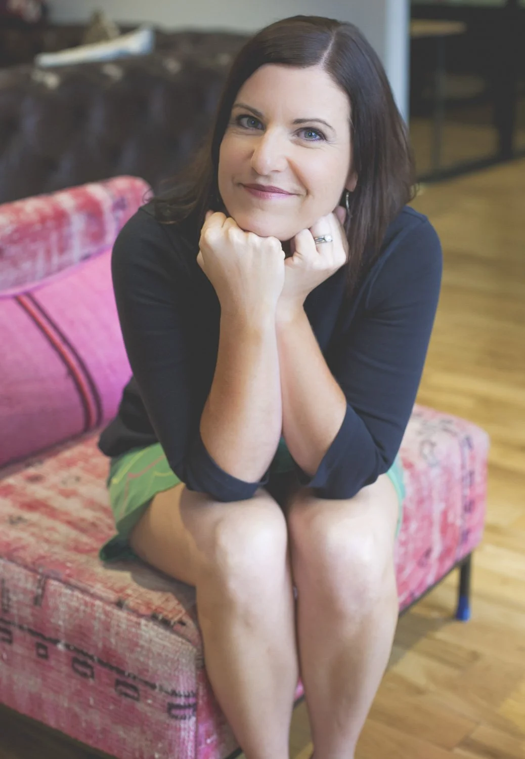 Rachel Muir beams with a warm smile, sitting on a vibrant, patterned pink chair, radiating the energy of a dedicated nonprofit fundraising consultant ready to make fundraising fun and effective.