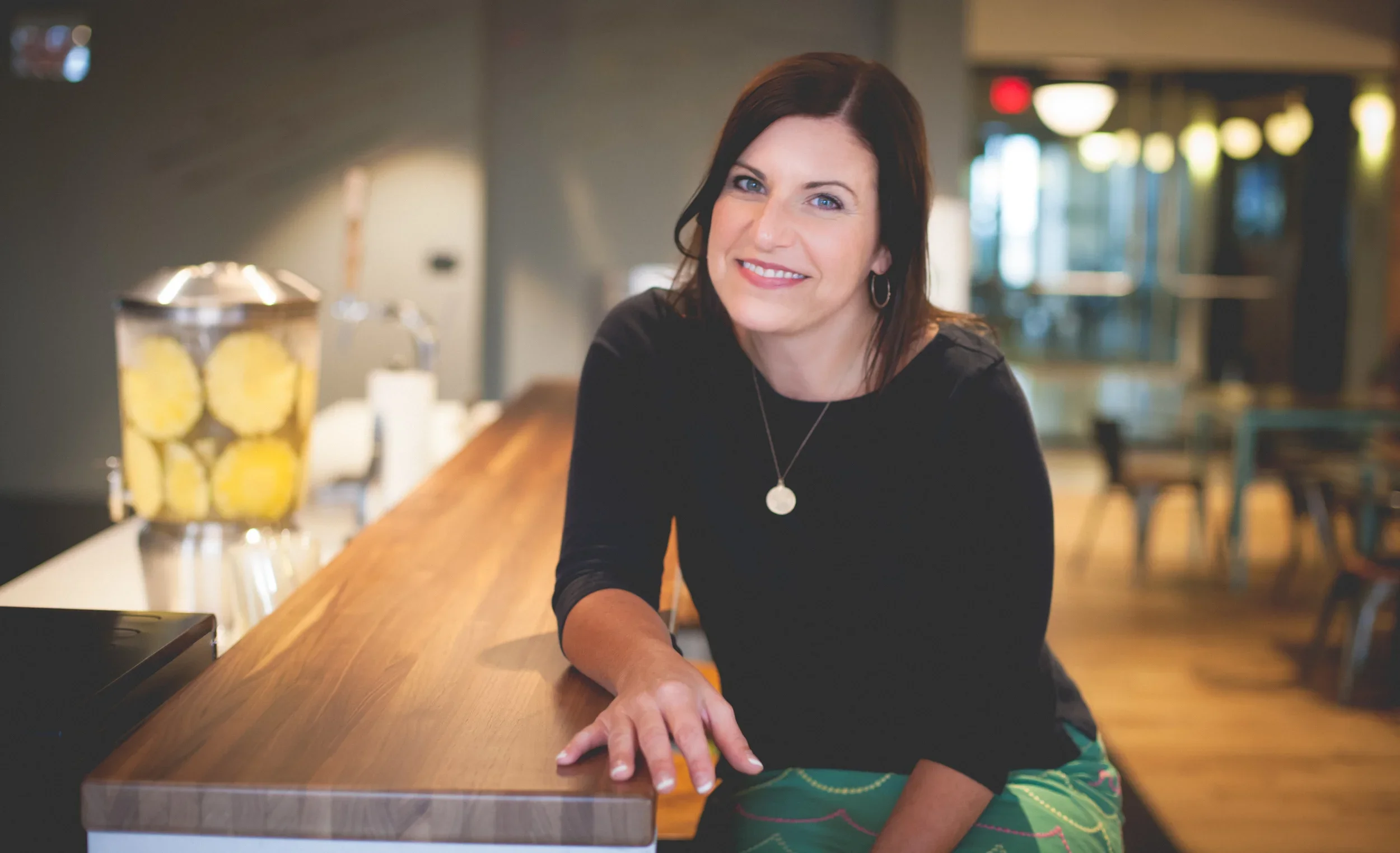 Rachel Muir, a warm and approachable nonprofit fundraising consultant, smiles at the camera, showcasing her vibrant green skirt and engaging presence against a cozy, modern backdrop.