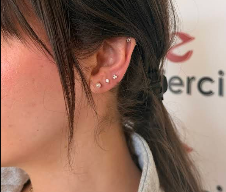 Close-up of a woman's left ear with three piercings, each decorated with small earrings, and a portion of her dark brown hair.