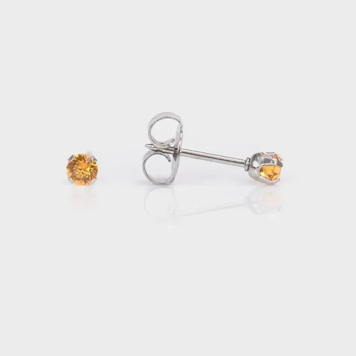 A pair of stud earrings with orange gemstones on a white background, one earring lying down and the other standing upright.