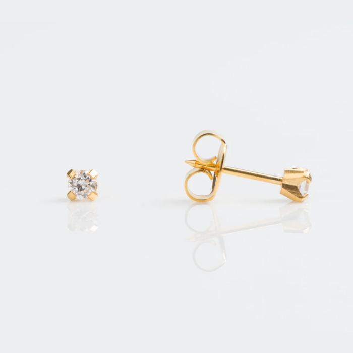 Gold stud earrings with clear gemstones on a white reflective surface.