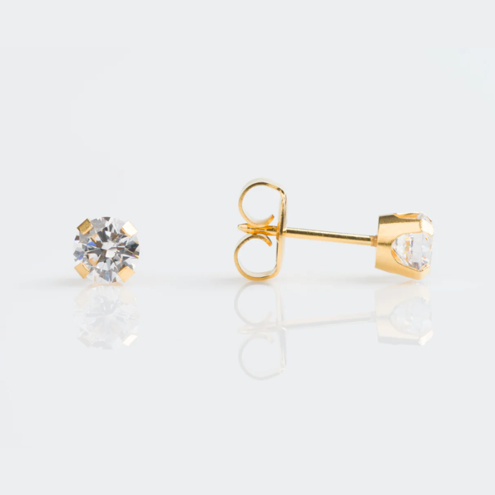 A pair of gold stud earrings with clear gemstones on a white reflective surface.