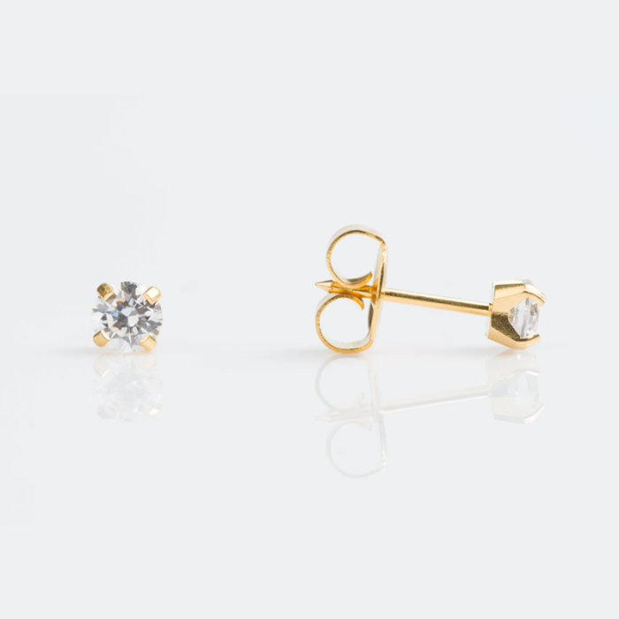 A pair of gold stud earrings with round clear gemstones on a white reflective surface.