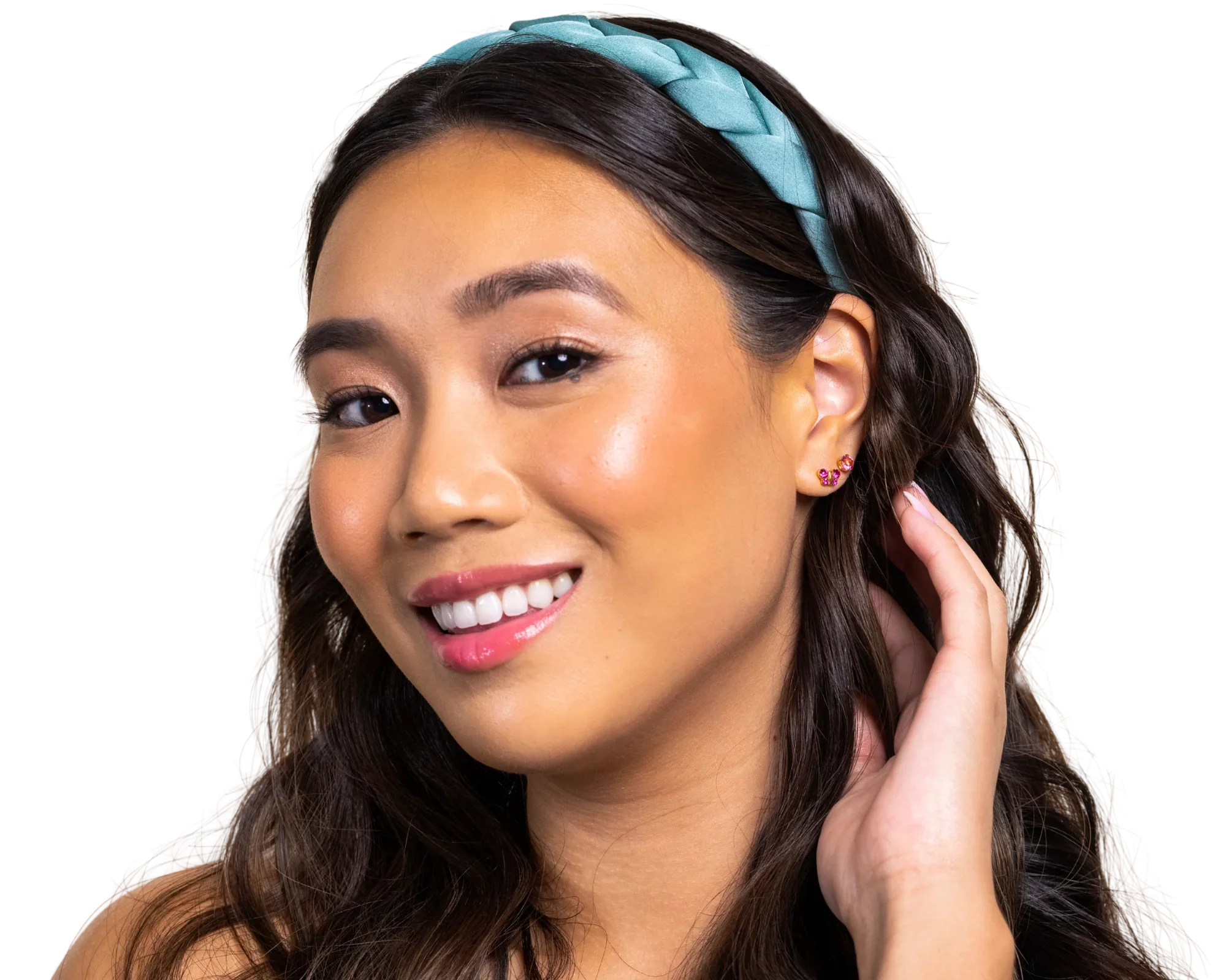 Close-up of a young woman's face, smiling, with dark hair styled in loose waves, wearing a blue braided headband, floral earrings, and makeup with pink lips.