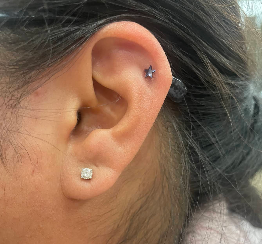 Close-up of a woman's ear with two earrings: a star-shaped earring in the upper ear and a diamond stud earring in the lower ear.