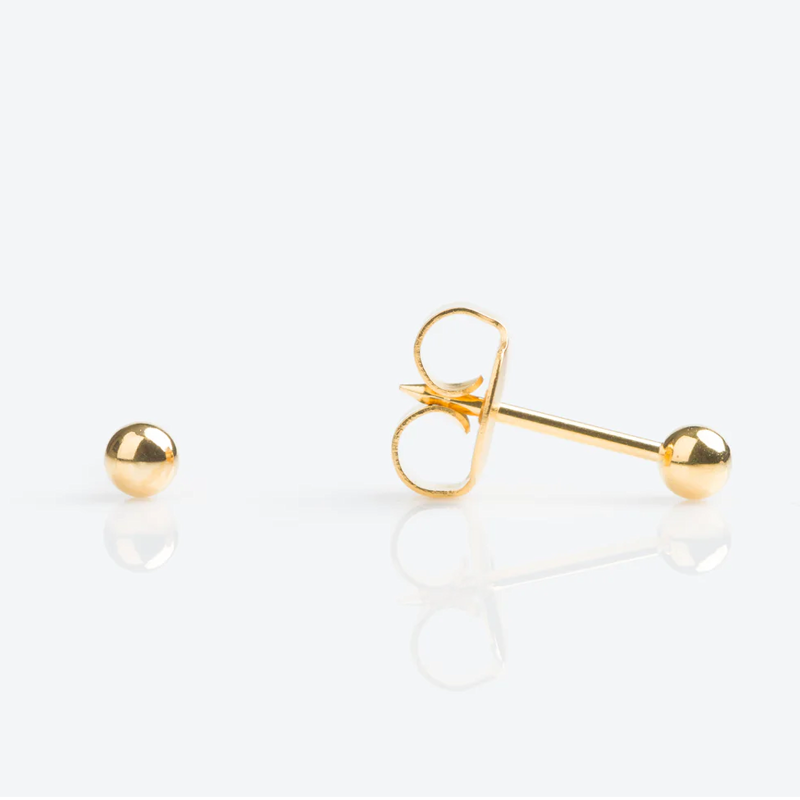 Close-up of a single gold stud earring with a spherical ball and a pair of gold hoop supports on a white reflective surface