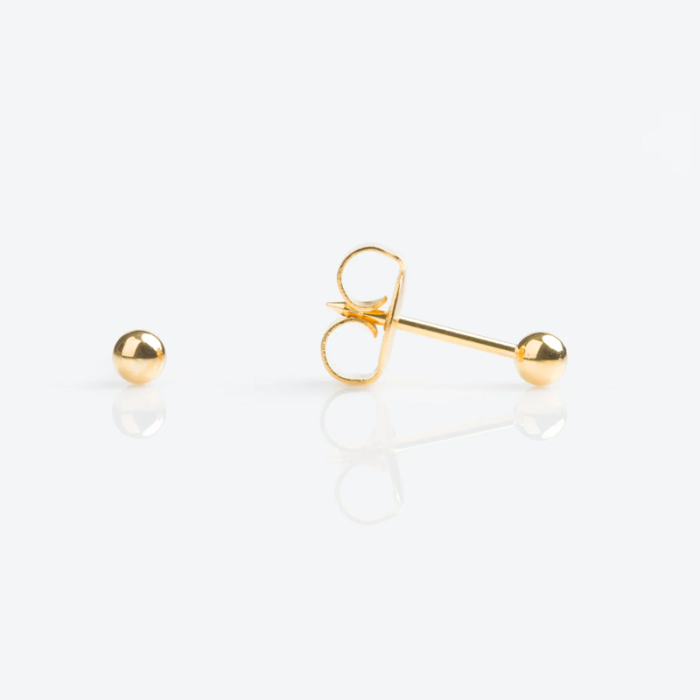 Close-up of a gold stud earring with a butterfly clasp and a separate gold ball backing on a white surface.
