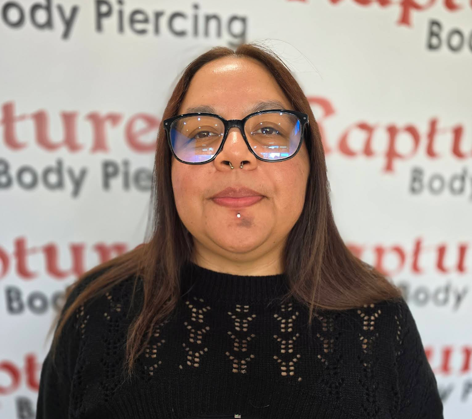 Woman with glasses and facial piercings, standing in front of a backdrop with the text 'Body Piercing' and 'Future'