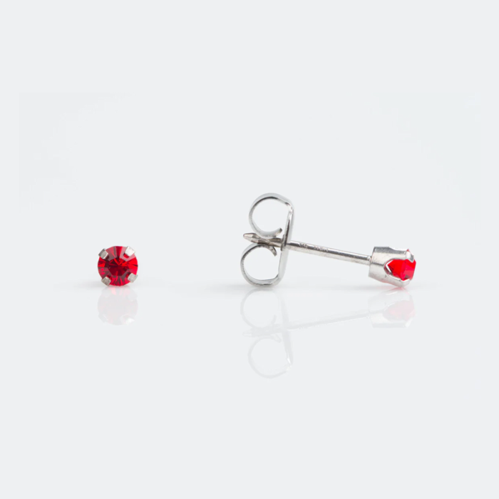 A pair of stud earrings with red gemstones on a white reflective surface.