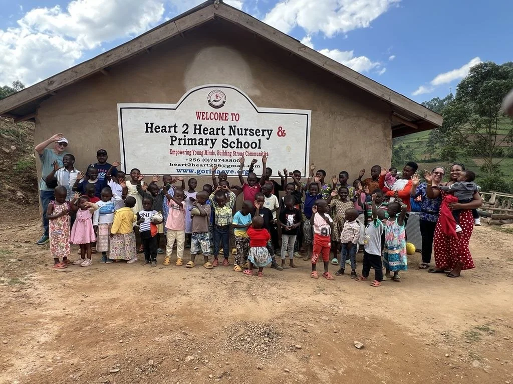 Bob and Gloria cooper standing with school children in front of  the Heart 2 Heart Nursery & Primary School in Uganda, Africa.