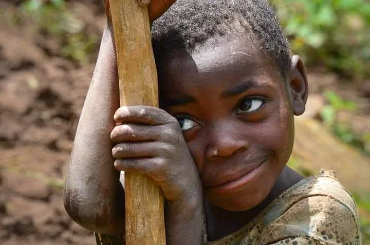 Little Batwa  boy in Uganda holding on to a staph and smiling