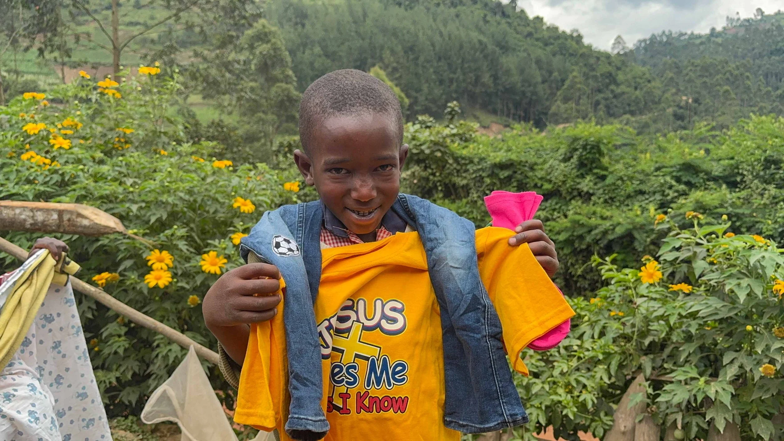 Batwa boy wearing a donated yellow shirt says Jesus loves me while smiling