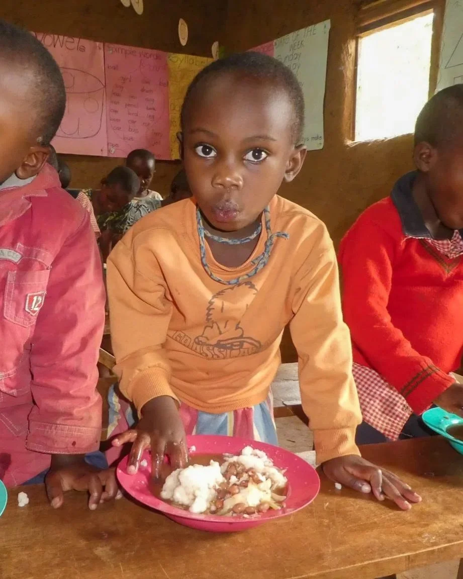 Little Batwa girl eating a donated meal at Christmas time in the Heart 2 Heart Primary School