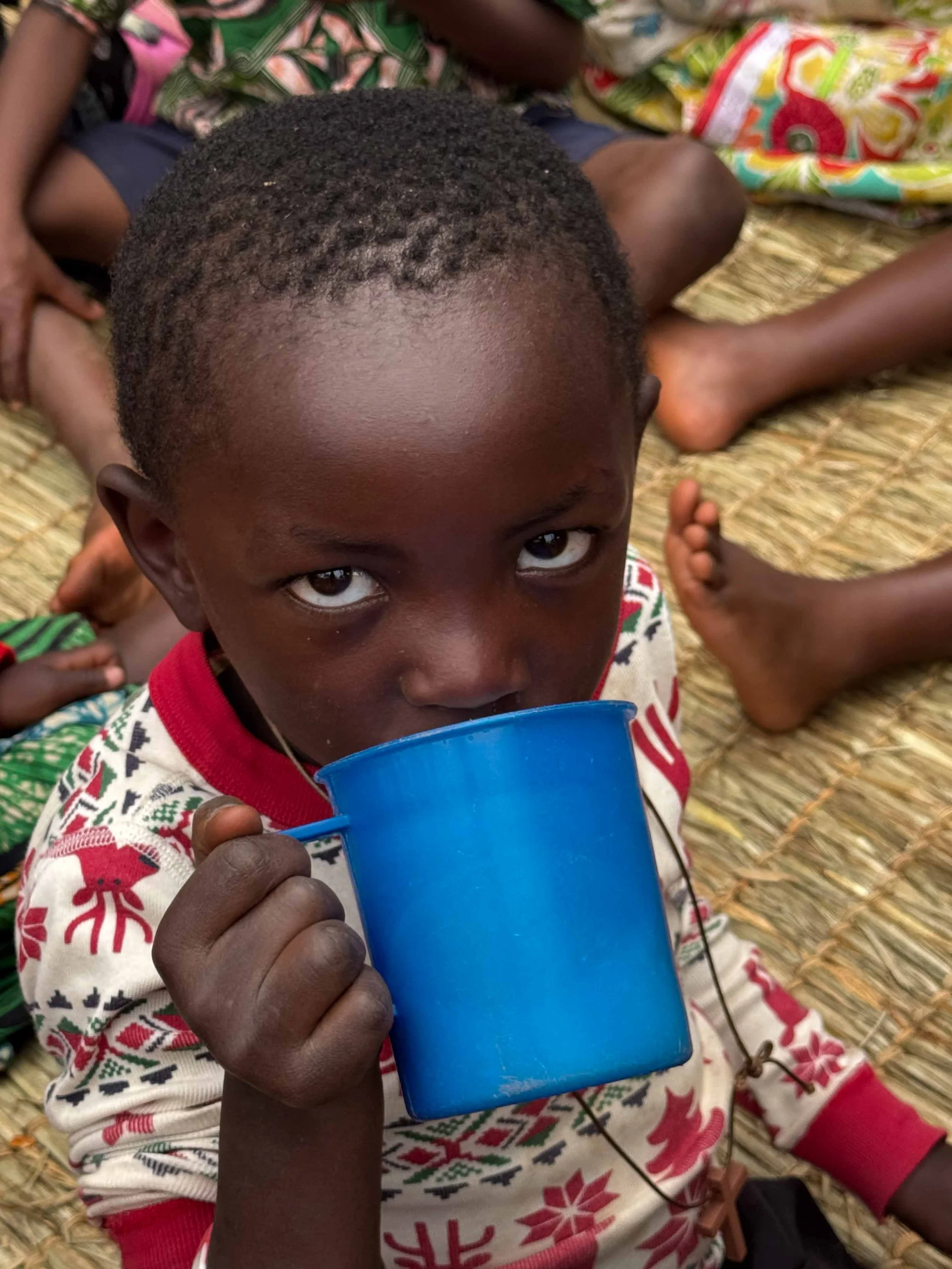 Young Batwa child drinking from a blue cup