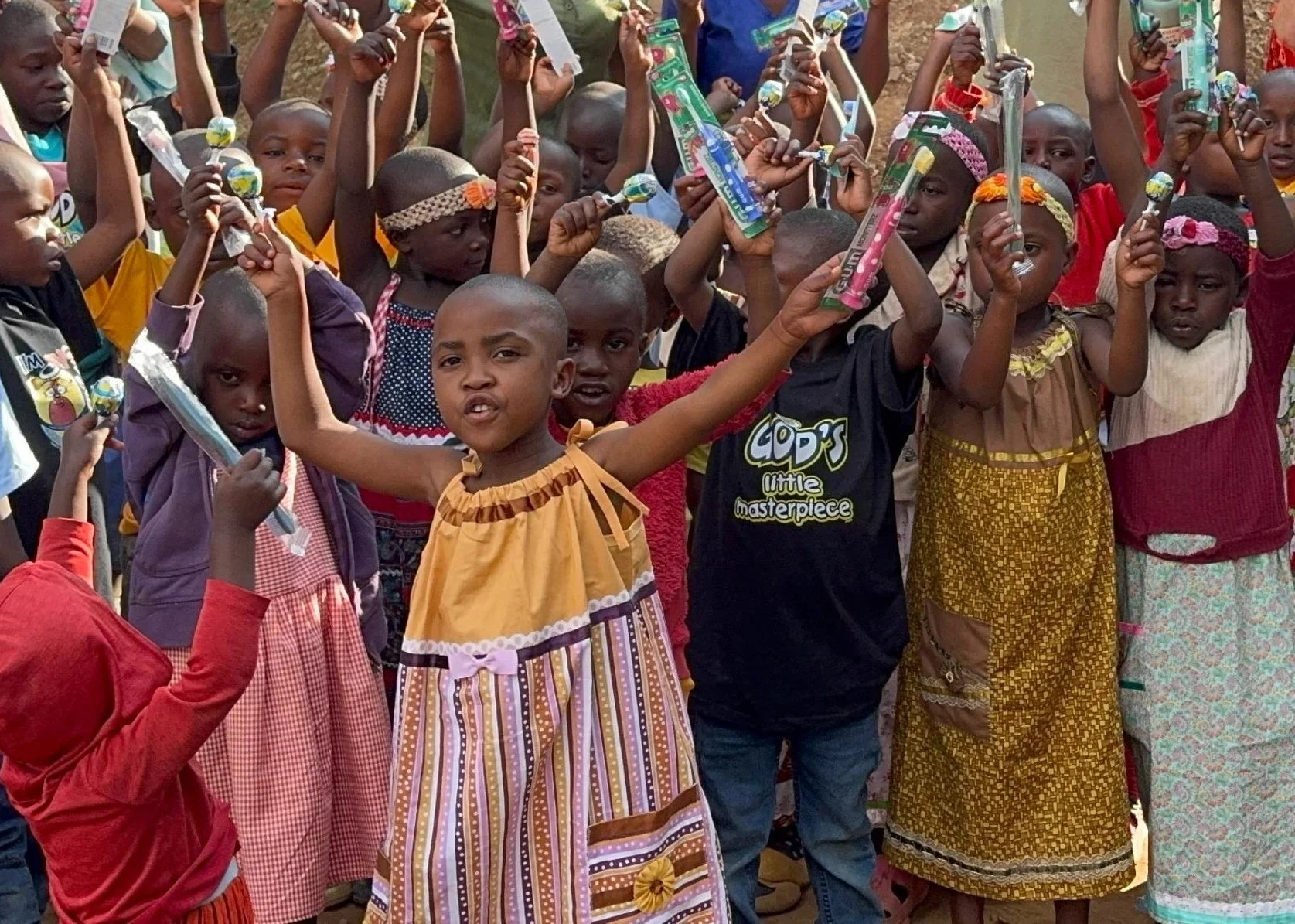 Batwa children smiling and holding up donated toothbrushes from H2HIntl made possible by your donations