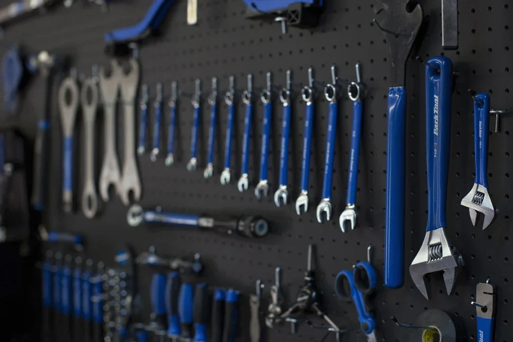 A black pegboard with various hand tools hanging, including wrenches, screwdrivers, pliers, and other small tools, organized in rows.