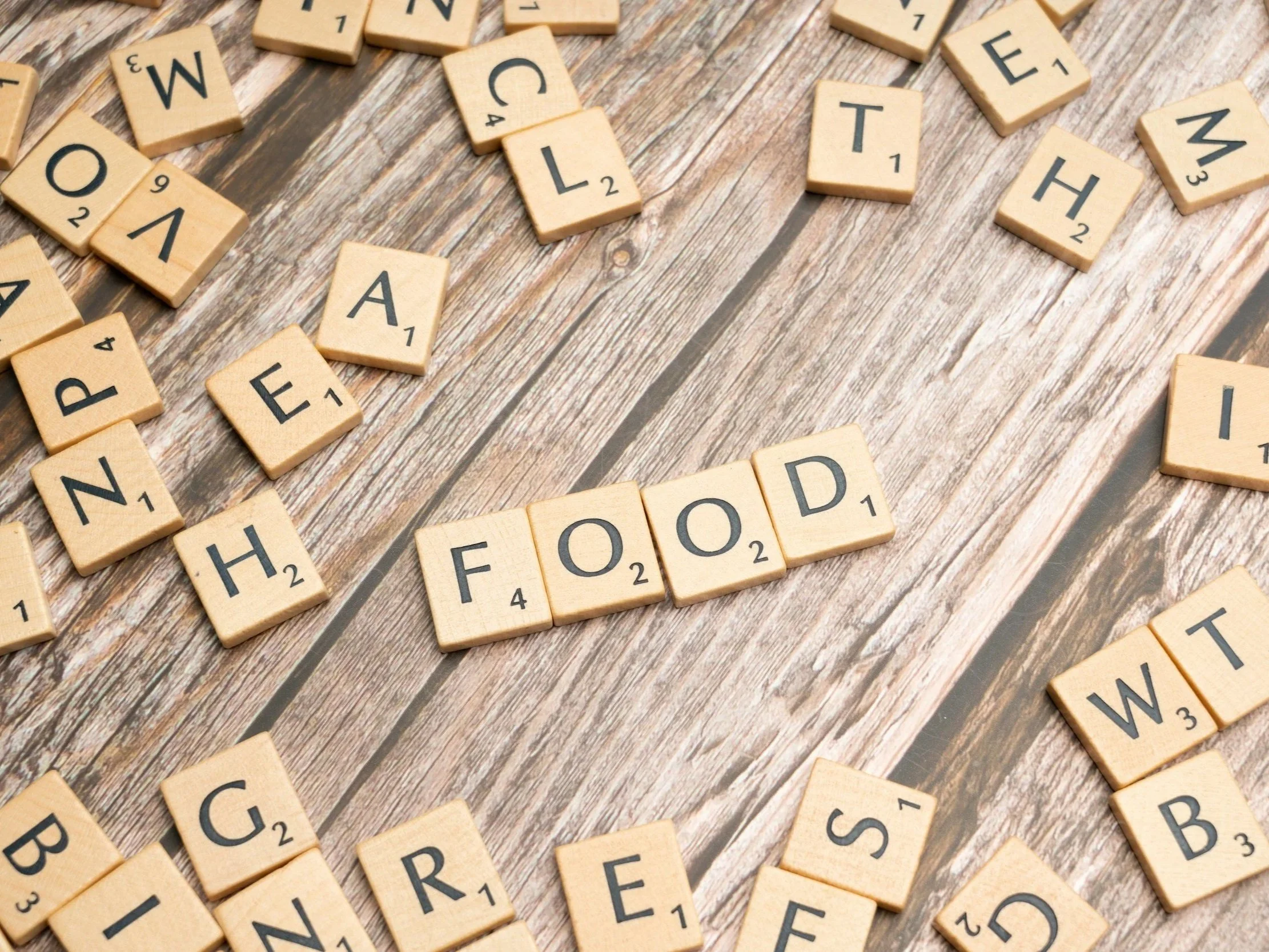 Scrabble tiles spelling out 'FOOD' on a wooden surface.