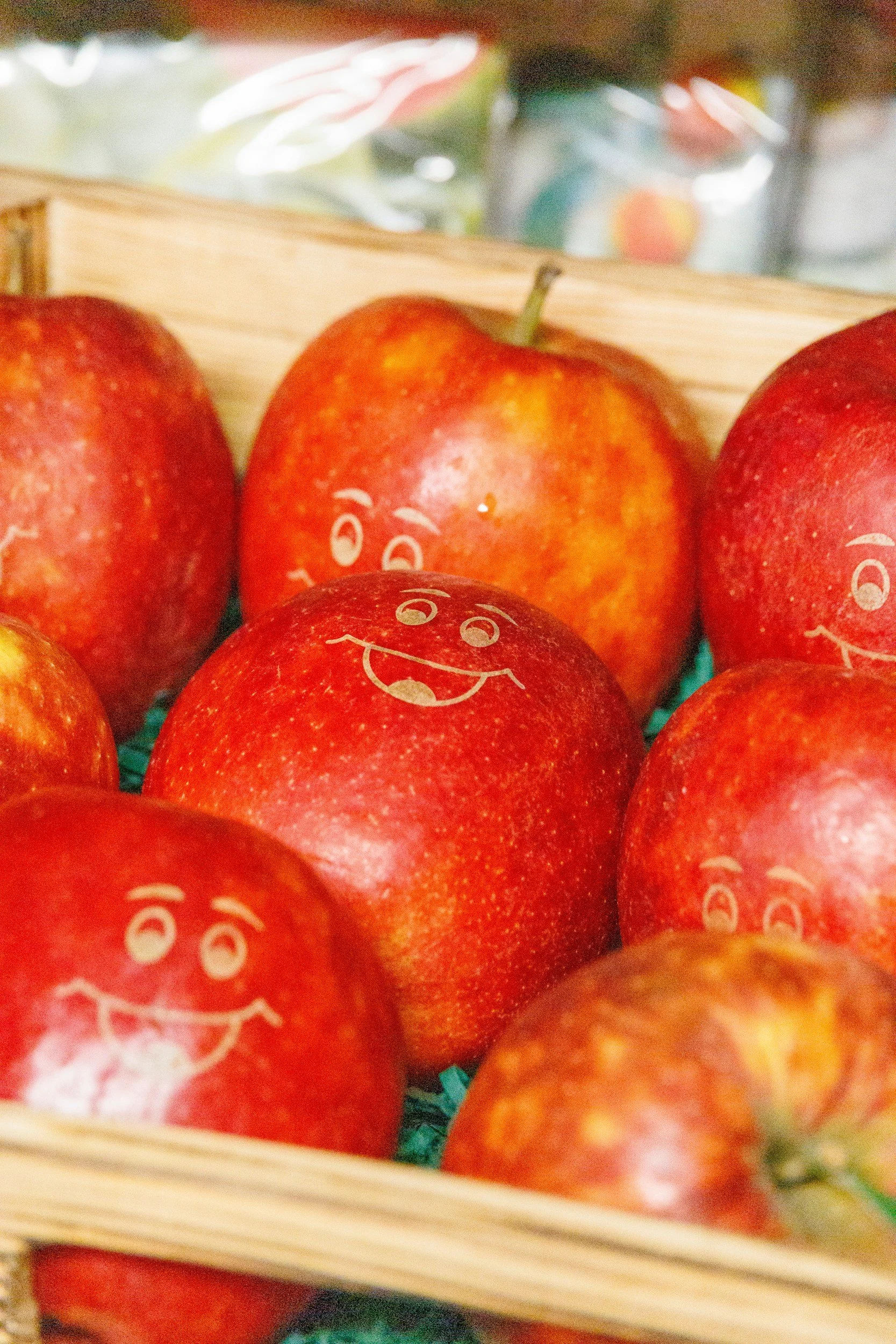 Red apples with smiley face drawings on them in a wooden basket.
