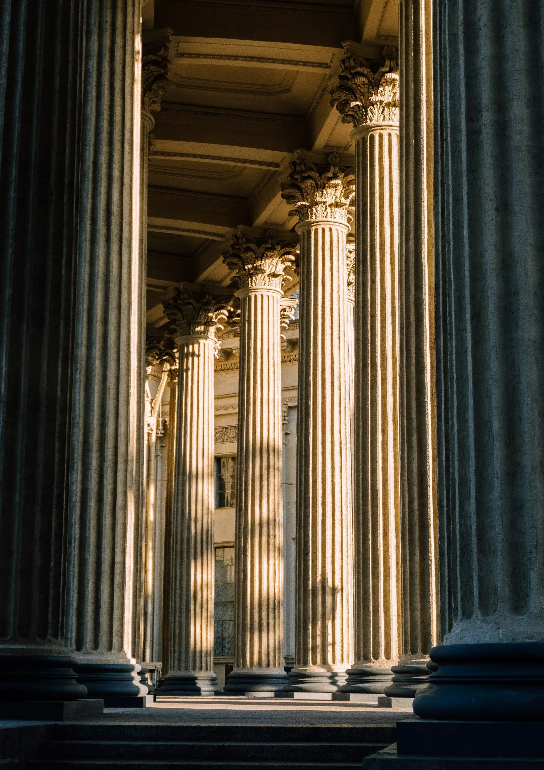 Ancient Greek or Roman temple entrance with tall, fluted columns and ornate capitals, illuminated by golden sunlight.