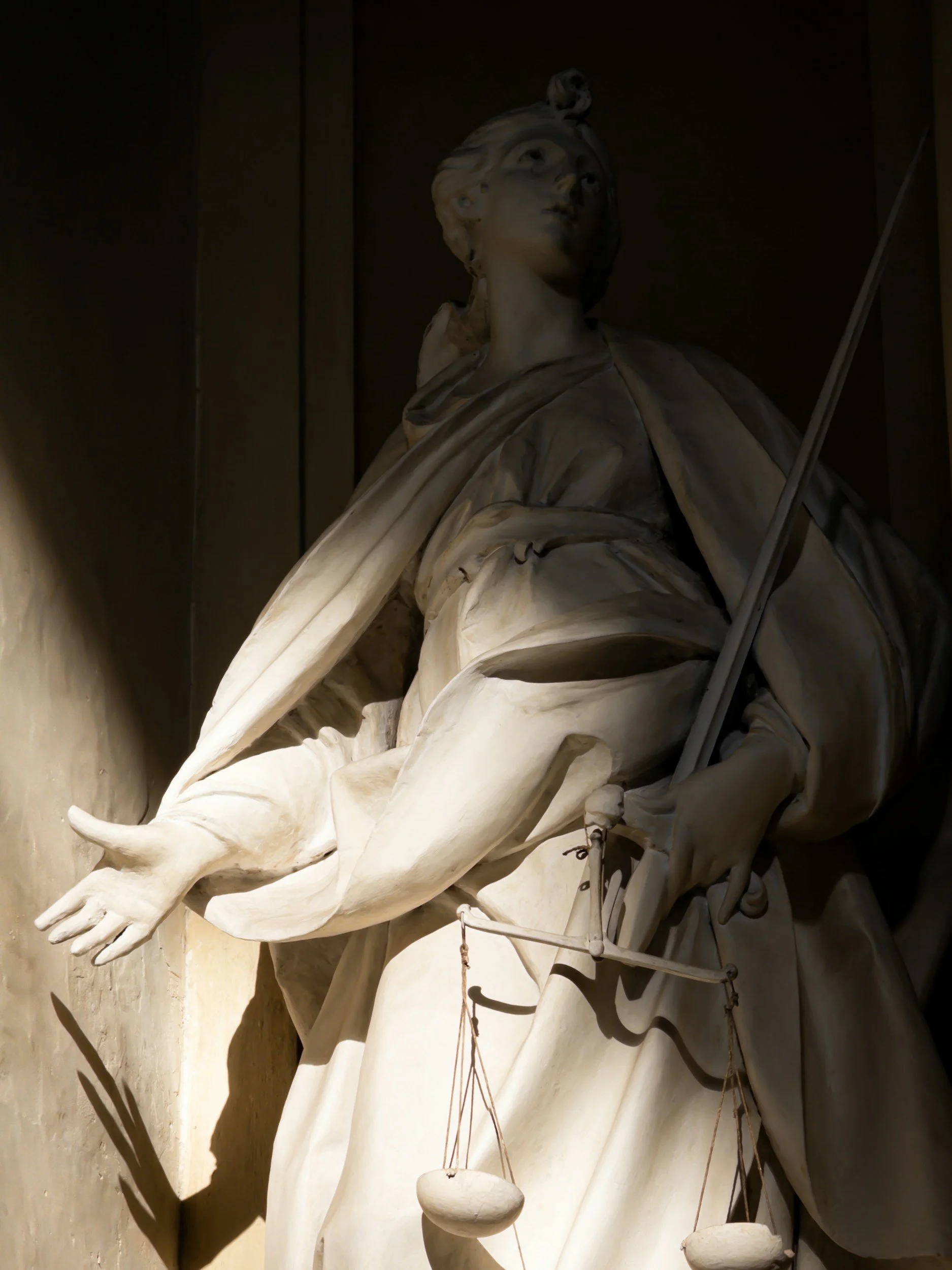 Close-up of a classical marble statue of a woman holding a scale and a sword, with dramatic lighting highlighting the sculpture's details.