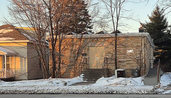 A residential house with a brick exterior, set against a backdrop of leafless trees and snow on the ground, in winter.