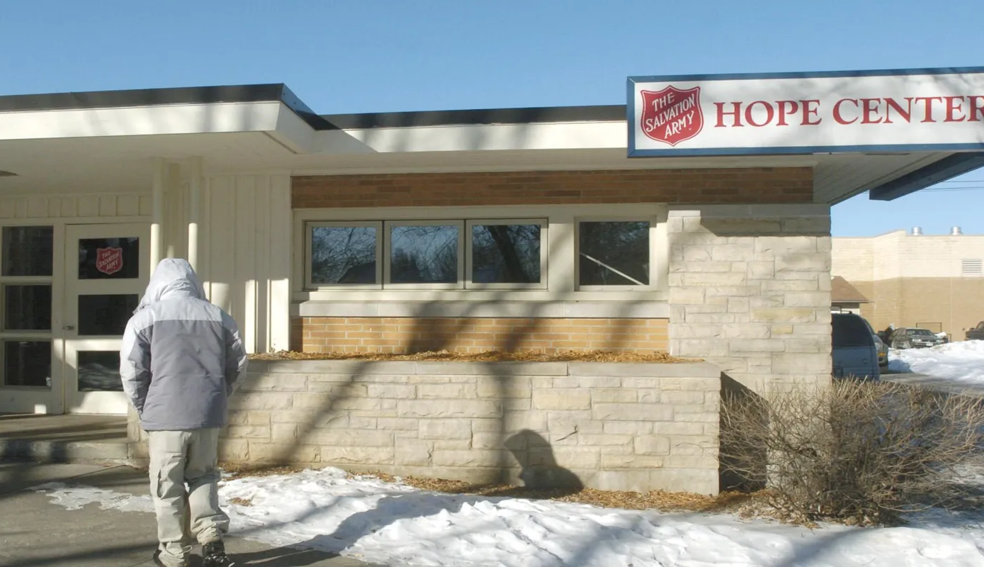 Person in a gray and white winter coat standing outside a Salvation Army Hope Center building on a snowy day.