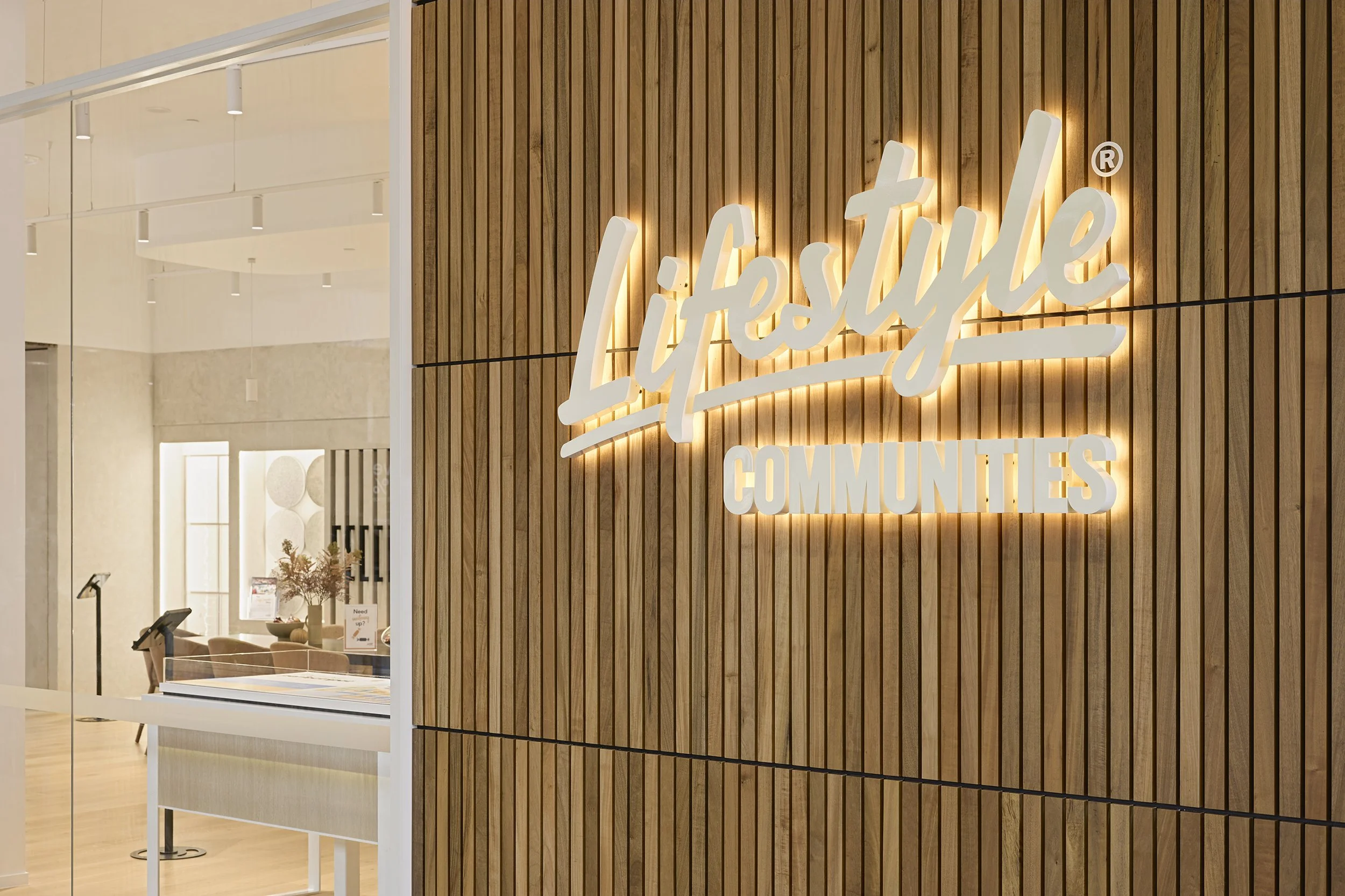 Lifestyle Communities illuminated signage featuring halo-lit fabricated lettering mounted on a timber slat wall, creating a premium internal branding display within a commercial fitout.