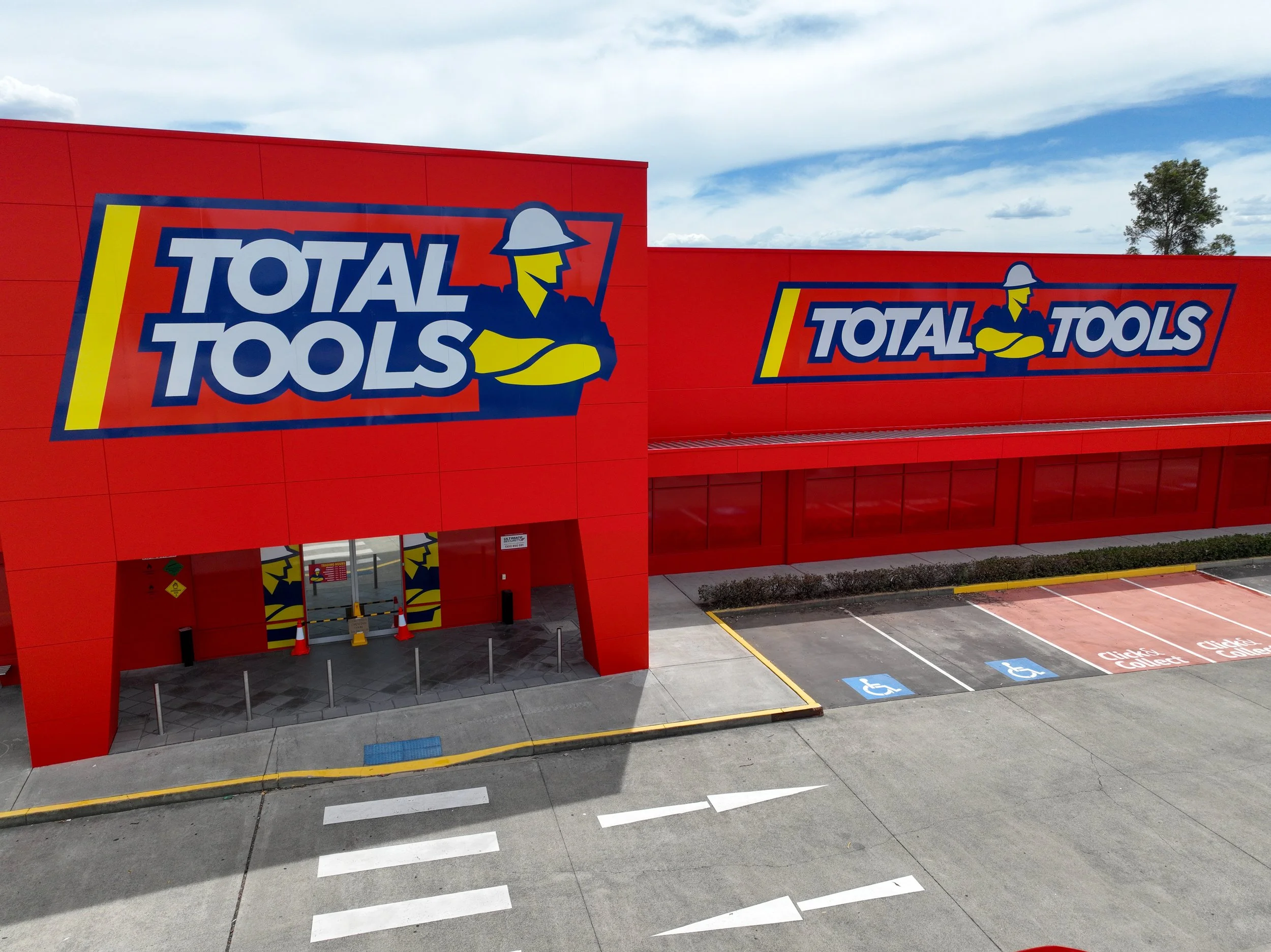 Total Tools storefront signage featuring large-format illuminated branding on red ACM cladding, installed across a commercial retail building facade with integrated entry signage and customer parking frontage.