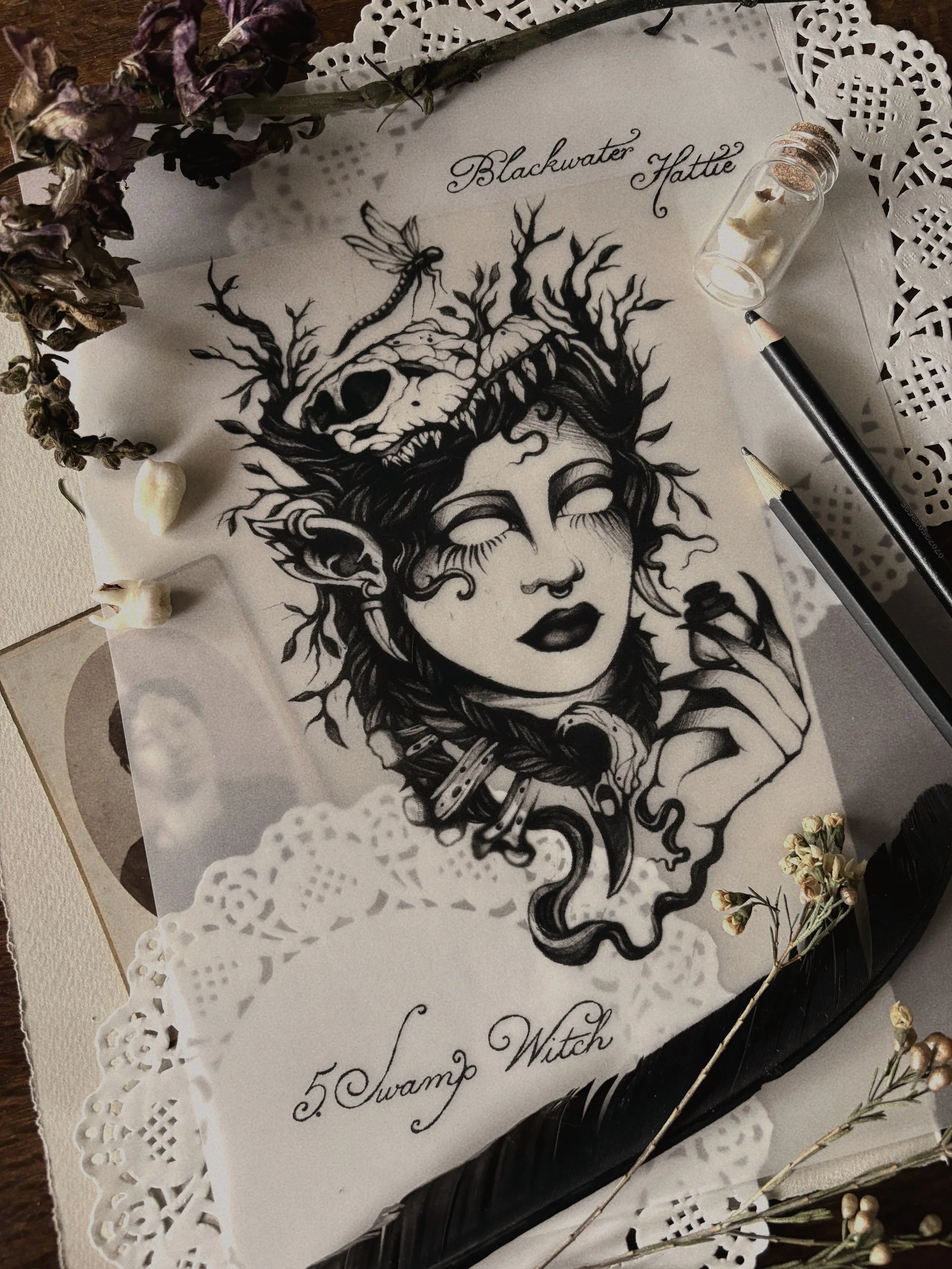 A black and white illustration of a woman with an elaborate hairstyle and floral elements, surrounded by dried flowers and a candle in a glass container, with handwritten text including the words "Blackwater Hattie" and "5 Swamp Witch."