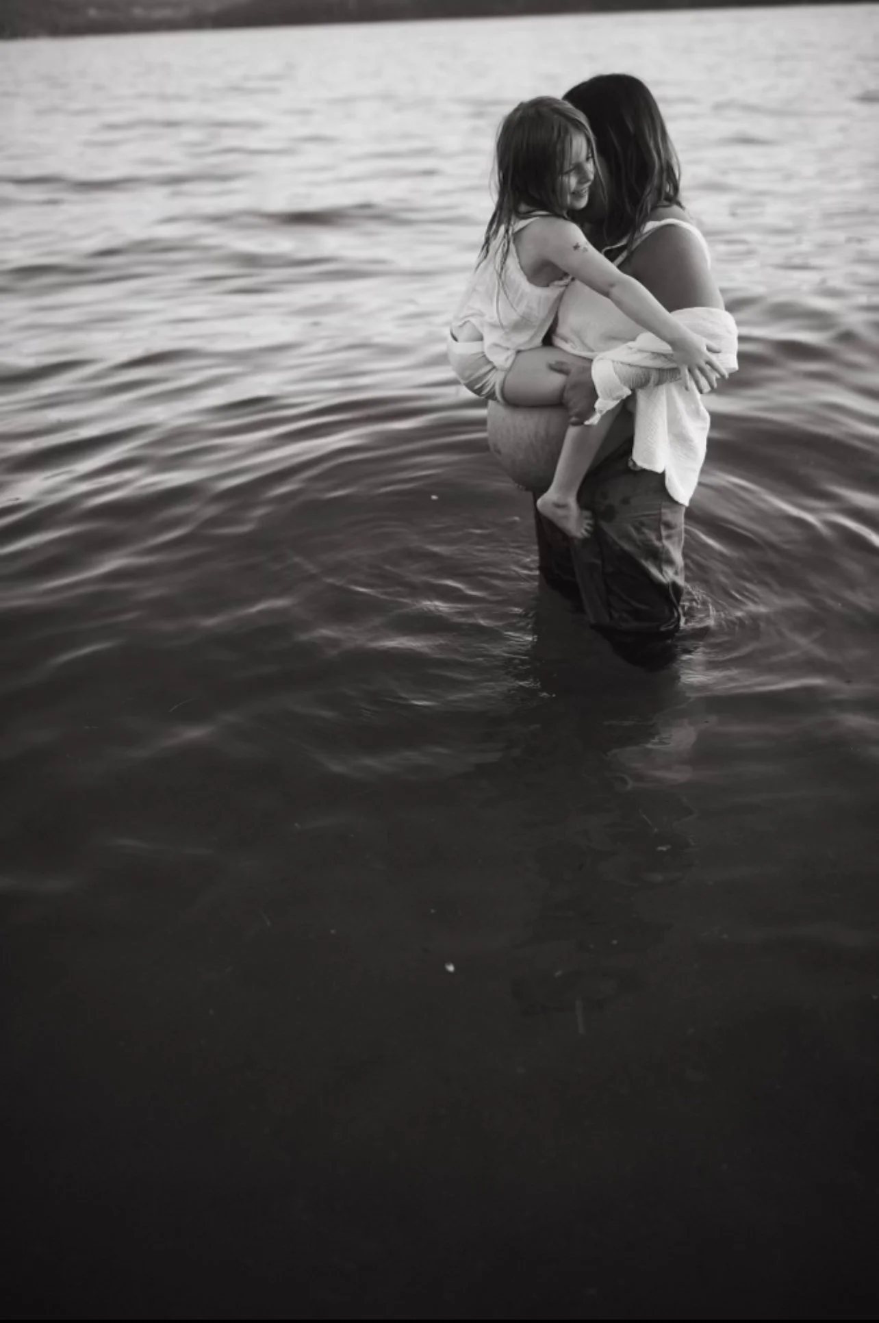 A woman holding a young girl in her arms in a body of water, smiling and enjoying the moment together.